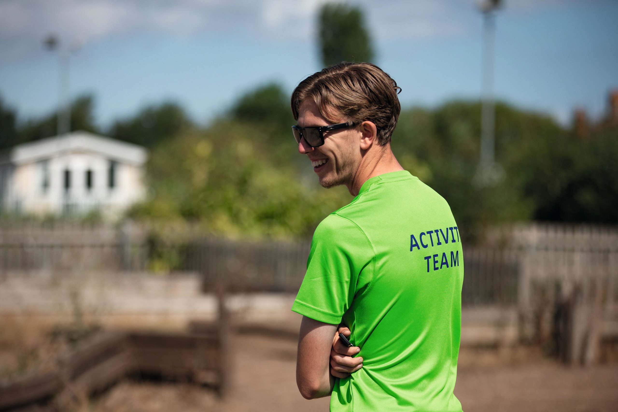 Smiling man in a bright green shirt with "ACTIVITY TEAM" on the back, wearing sunglasses outdoors.