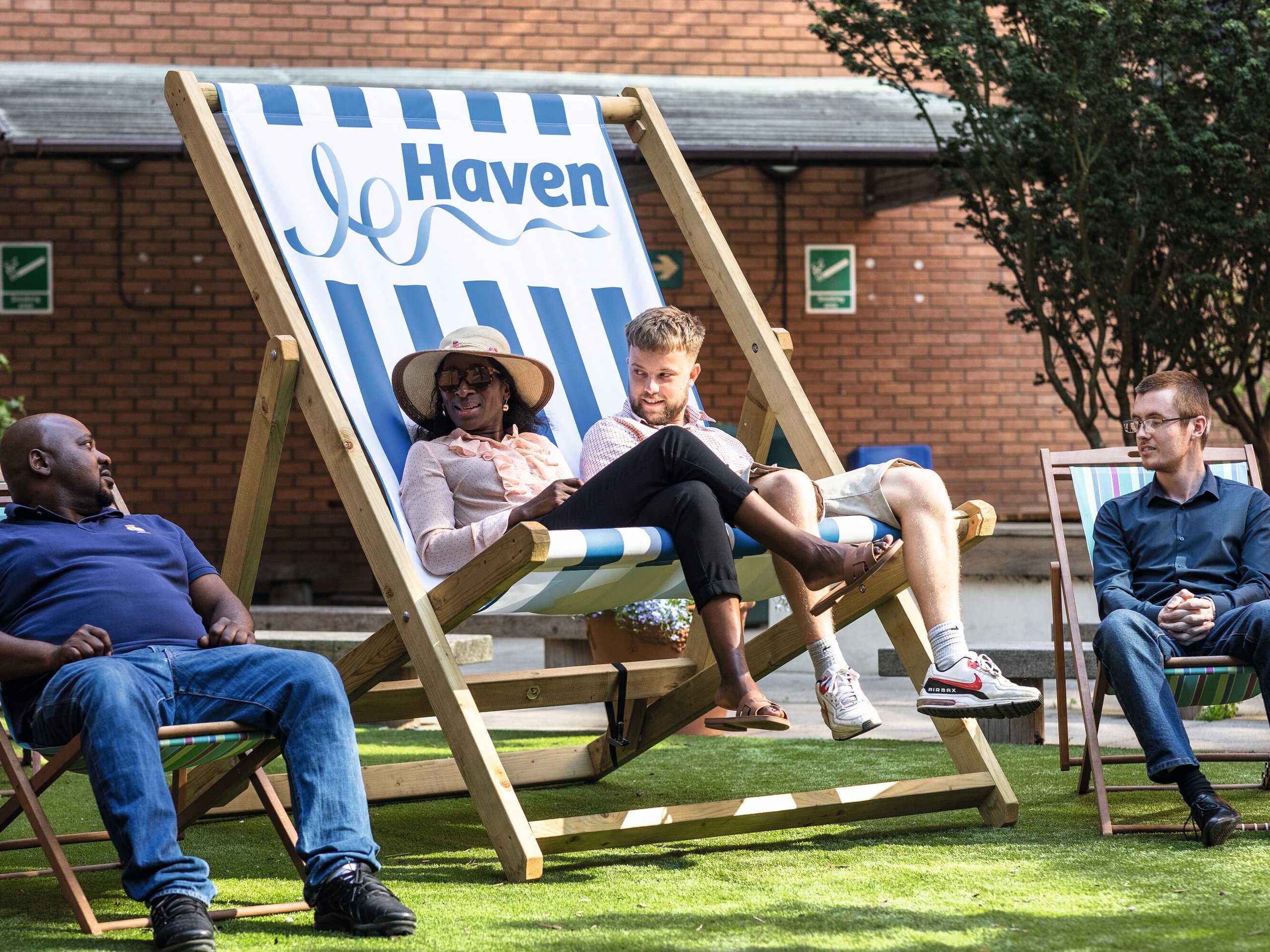 Colleagues relax on deckchairs in a sunny garden area outside an office building, with the "Haven" logo visible on one deckchair.