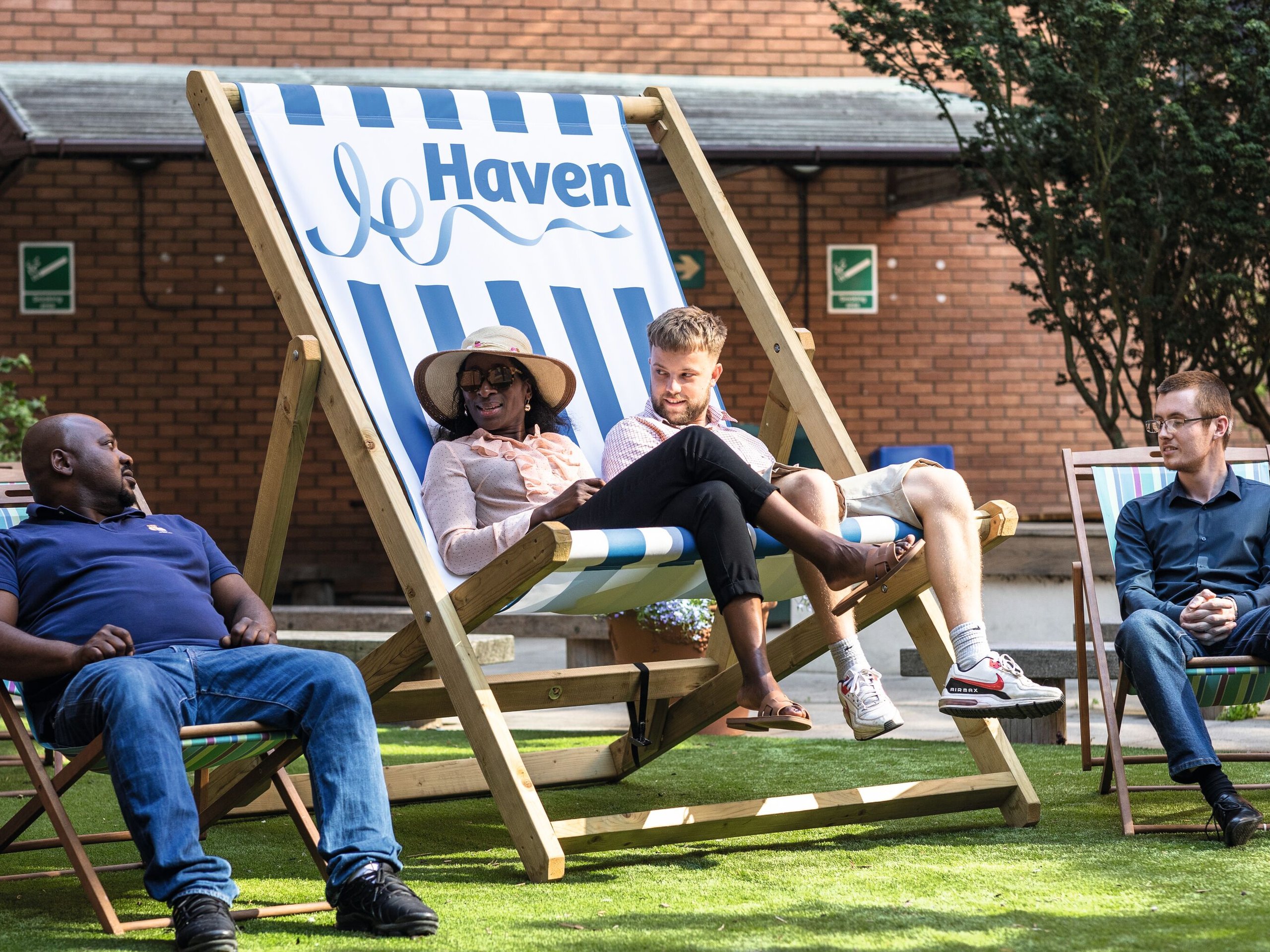 Colleagues relax on deckchairs in a sunny garden area outside an office building, with the "Haven" logo visible on one deckchair.