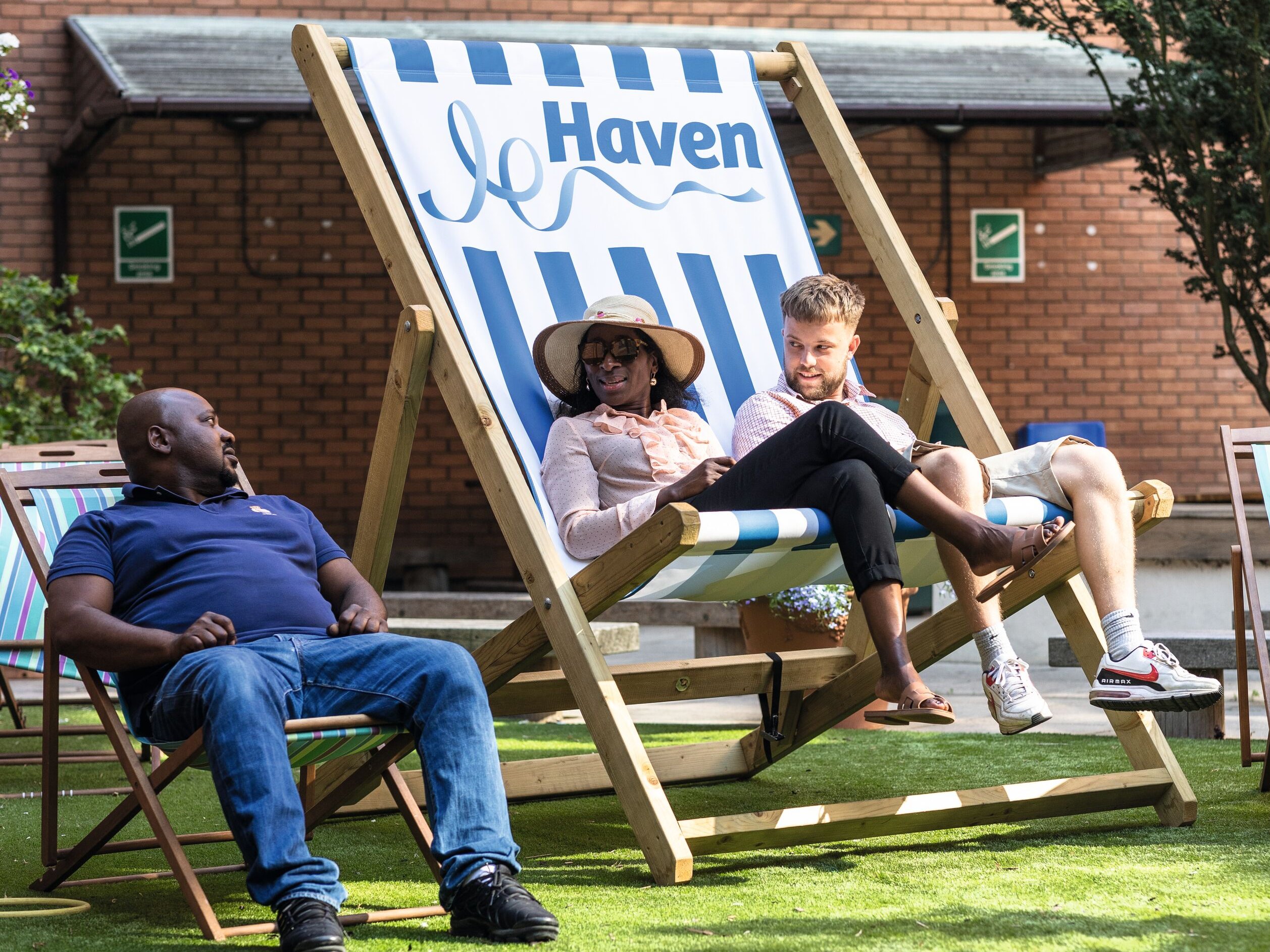 Colleagues relax on deckchairs in a sunny garden area outside an office building, with the "Haven" logo visible on one deckchair.