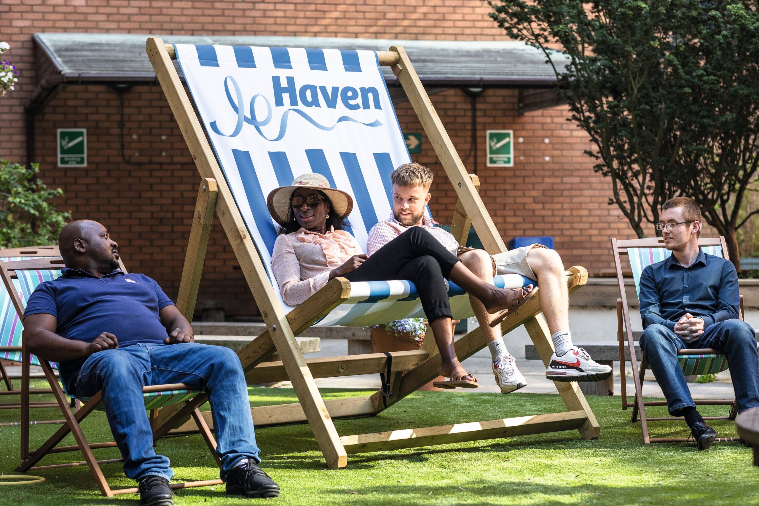 Colleagues relax on deckchairs in a sunny garden area outside an office building, with the "Haven" logo visible on one deckchair.