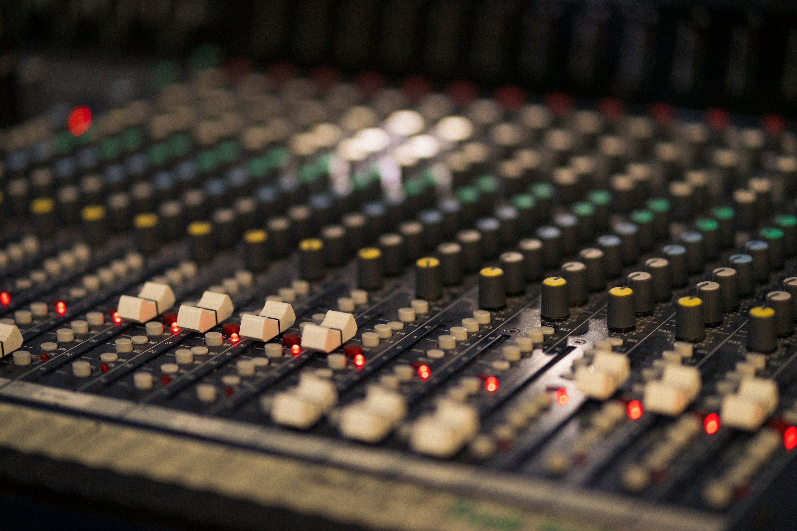 A close-up view of a professional audio mixing desk with illuminated buttons and faders.