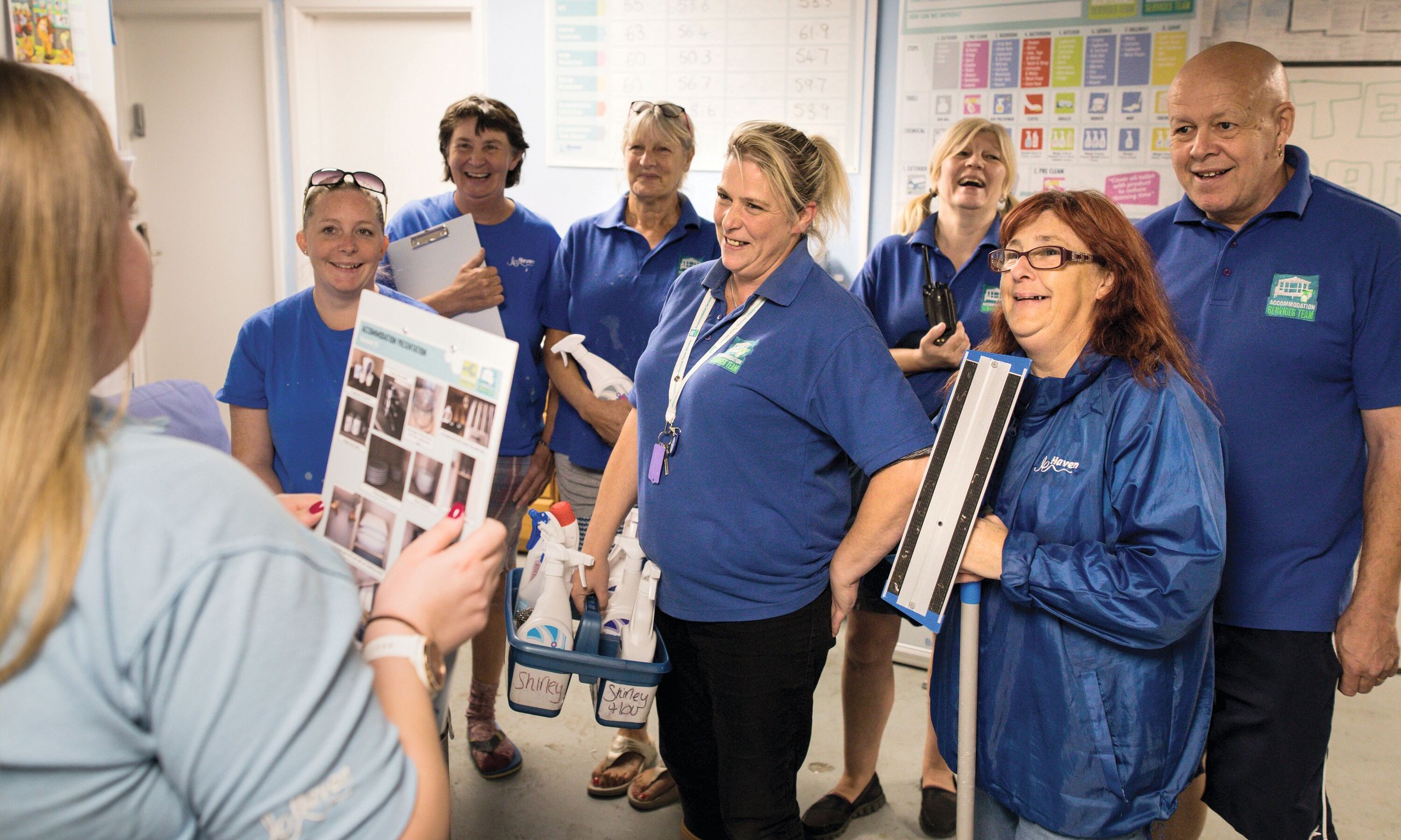 A group of housekeepers in blue uniforms attending a training session with cleaning supplies.