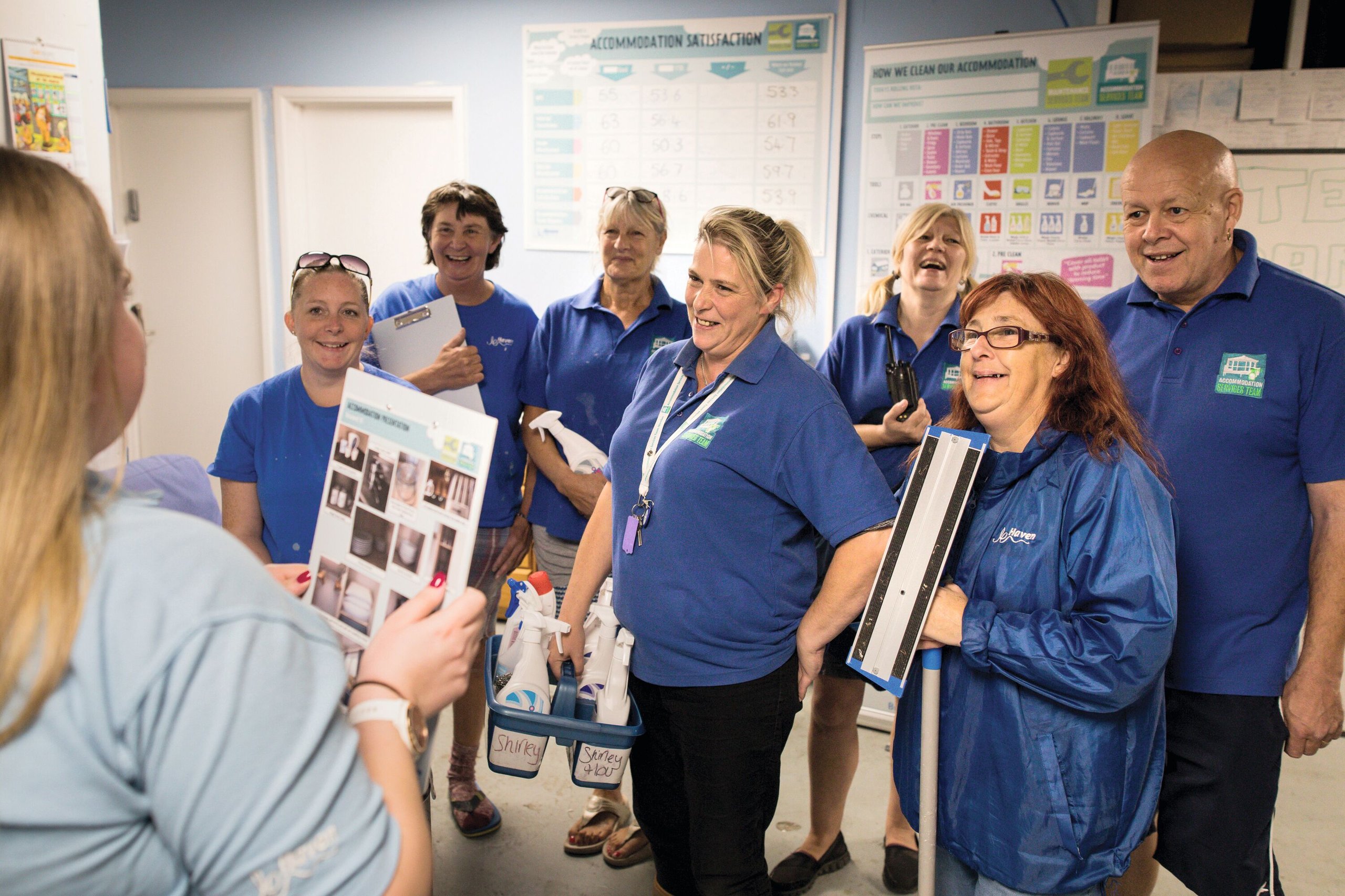A group of housekeepers in blue uniforms attending a training session with cleaning supplies.