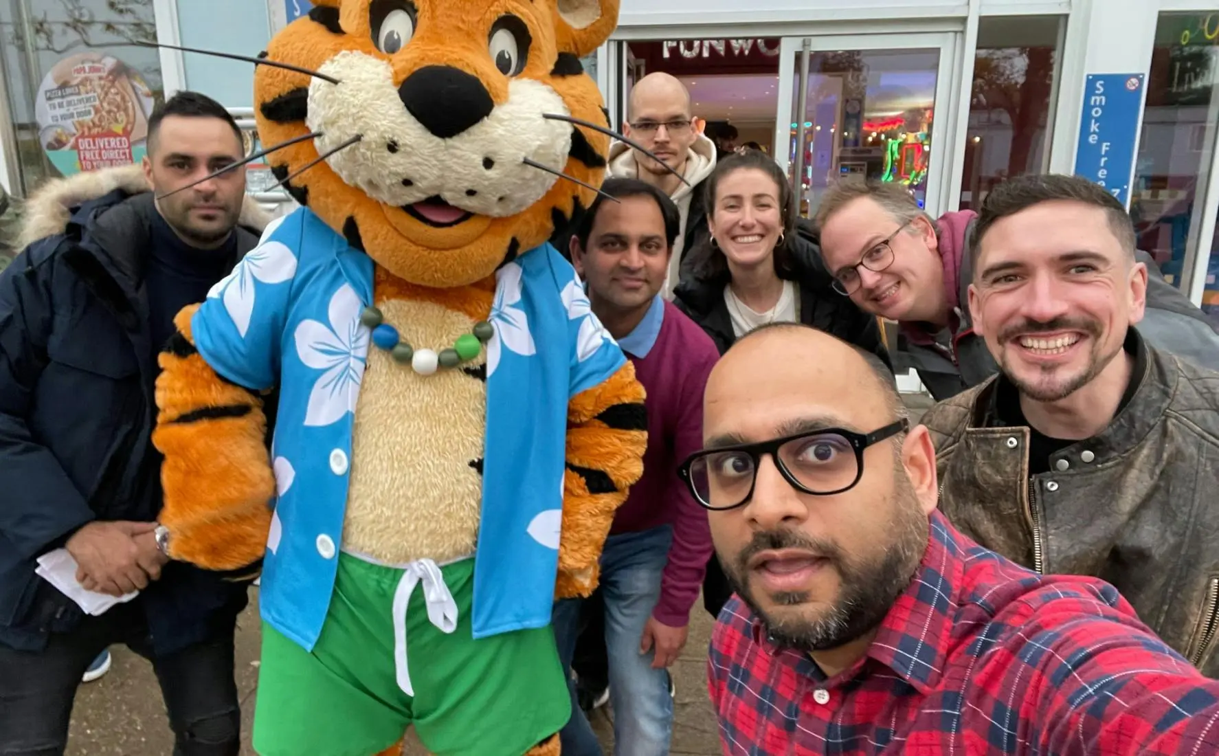 A diverse group of colleagues taking a selfie with a person in a tiger mascot costume.