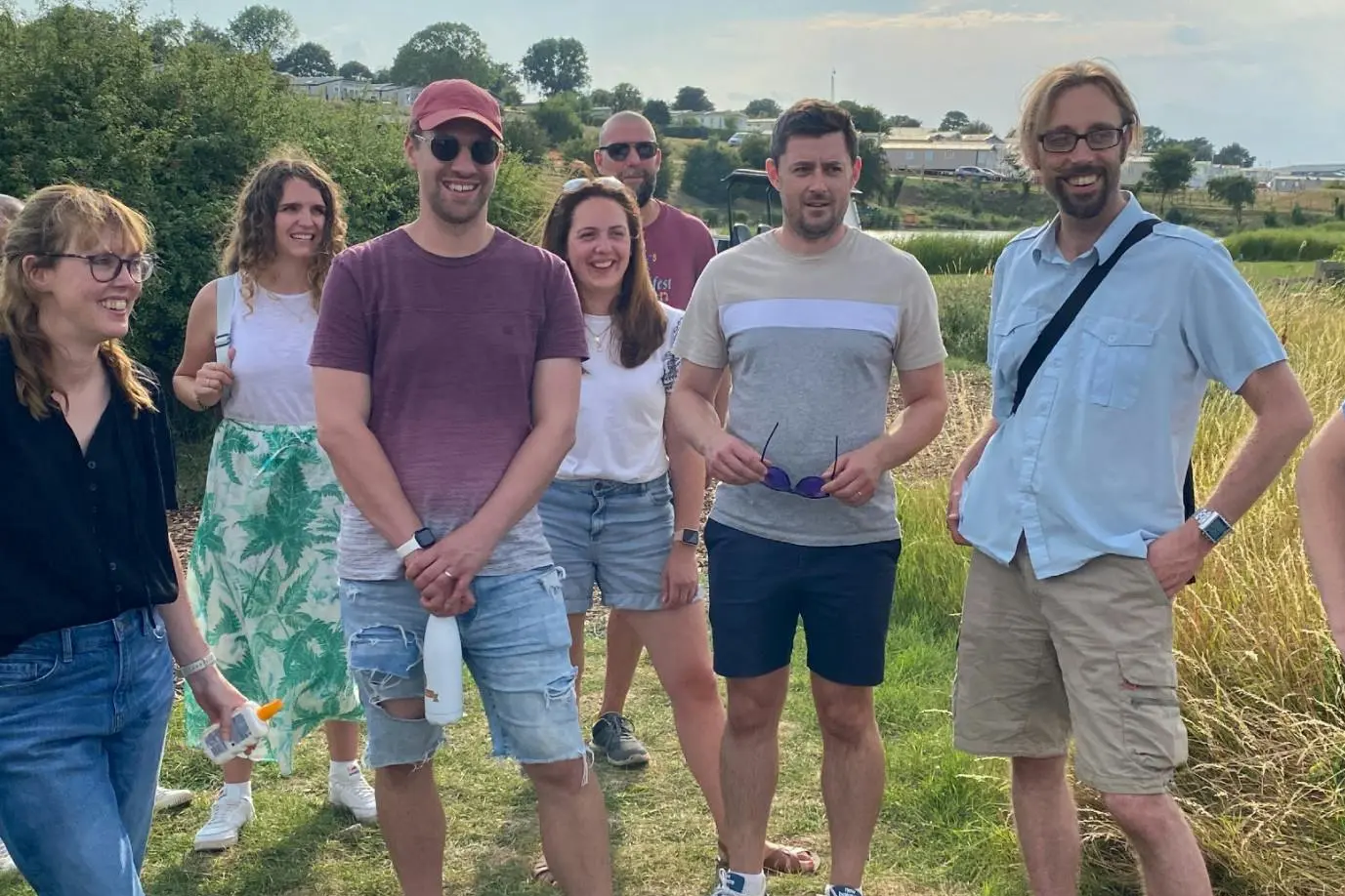 A group of friends standing in a grassy field during a sunny day.
