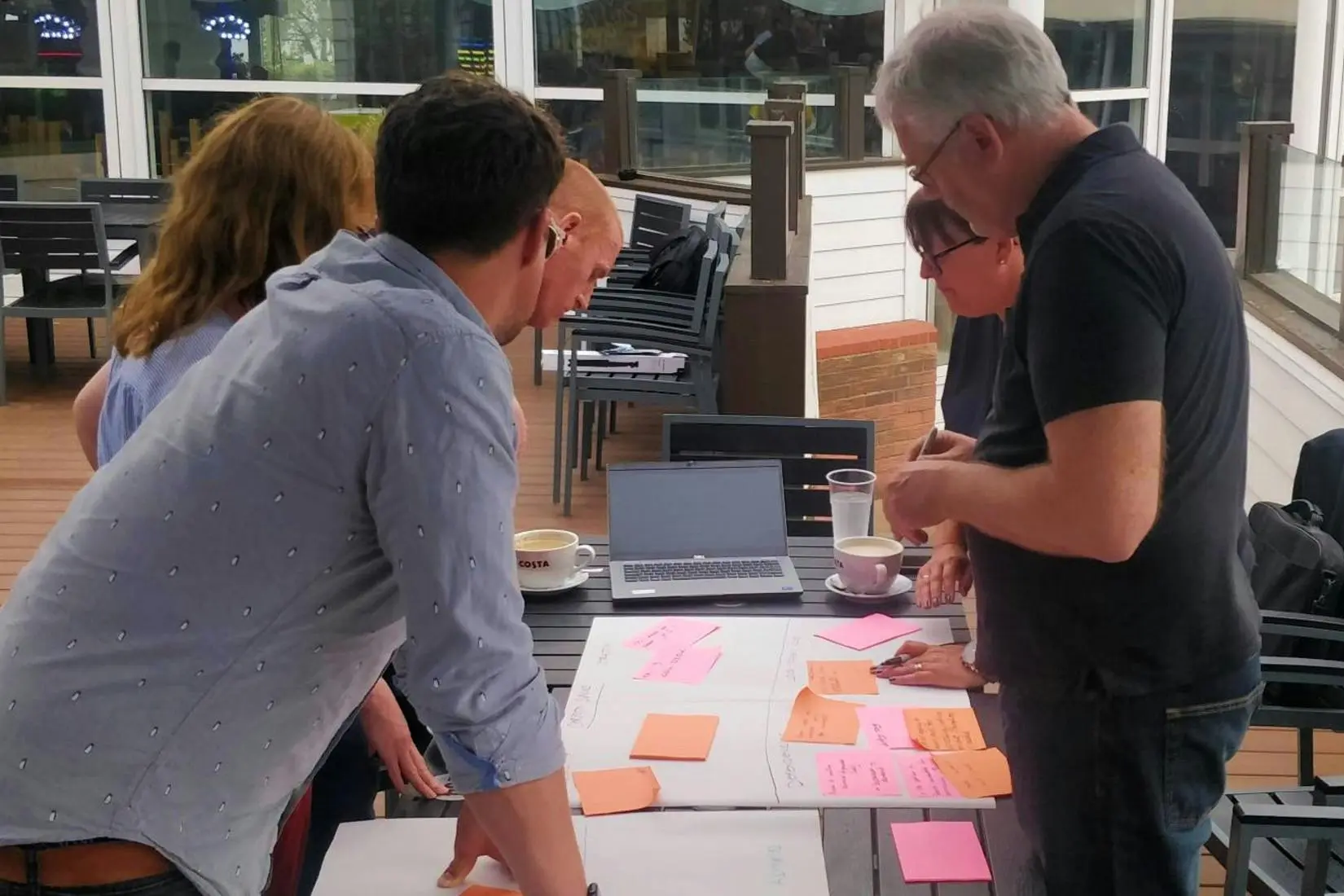 A group of colleagues collaborating on a project with sticky notes and a laptop at an outdoor table.