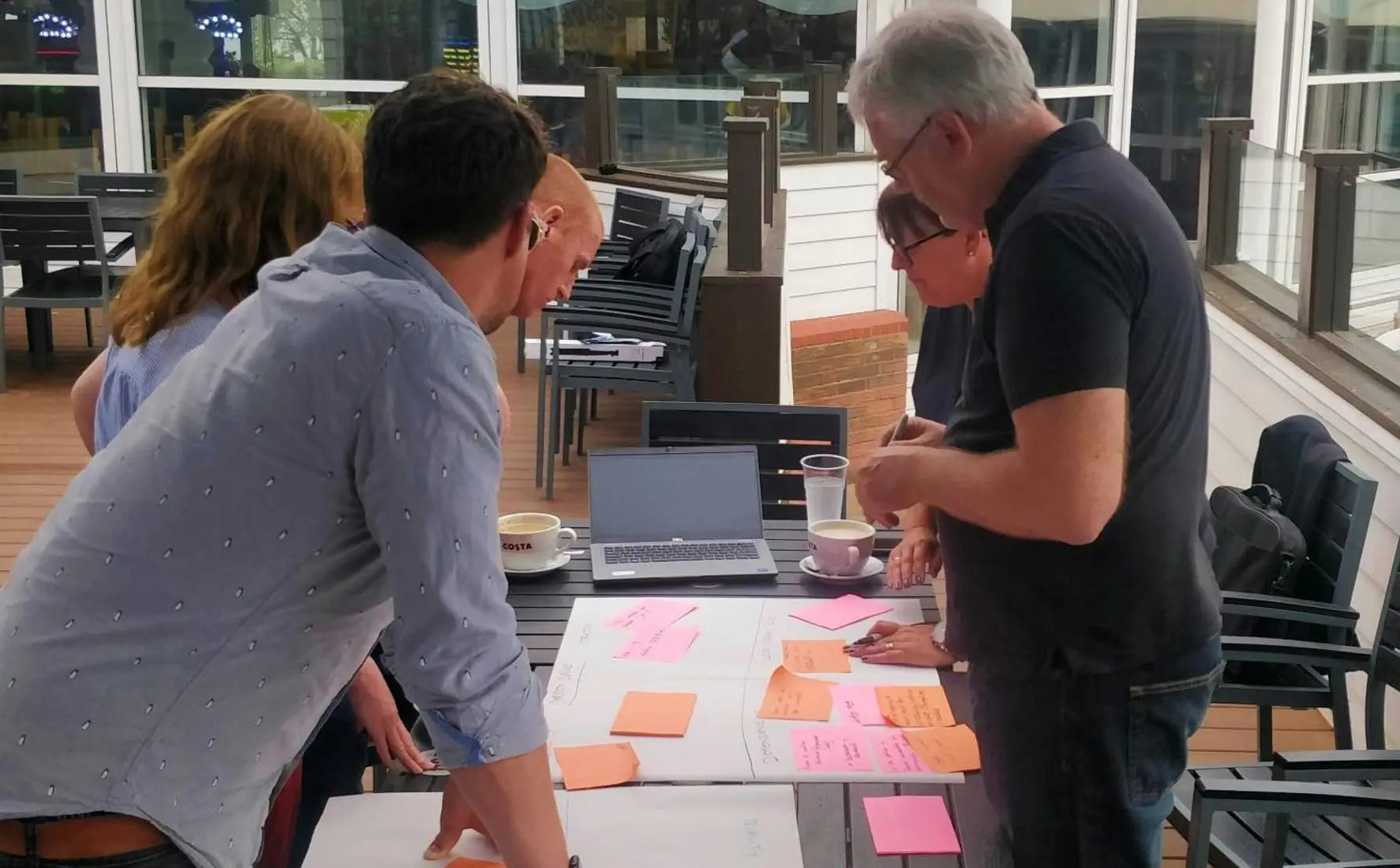A group of colleagues collaborating on a project with sticky notes and a laptop at an outdoor table.
