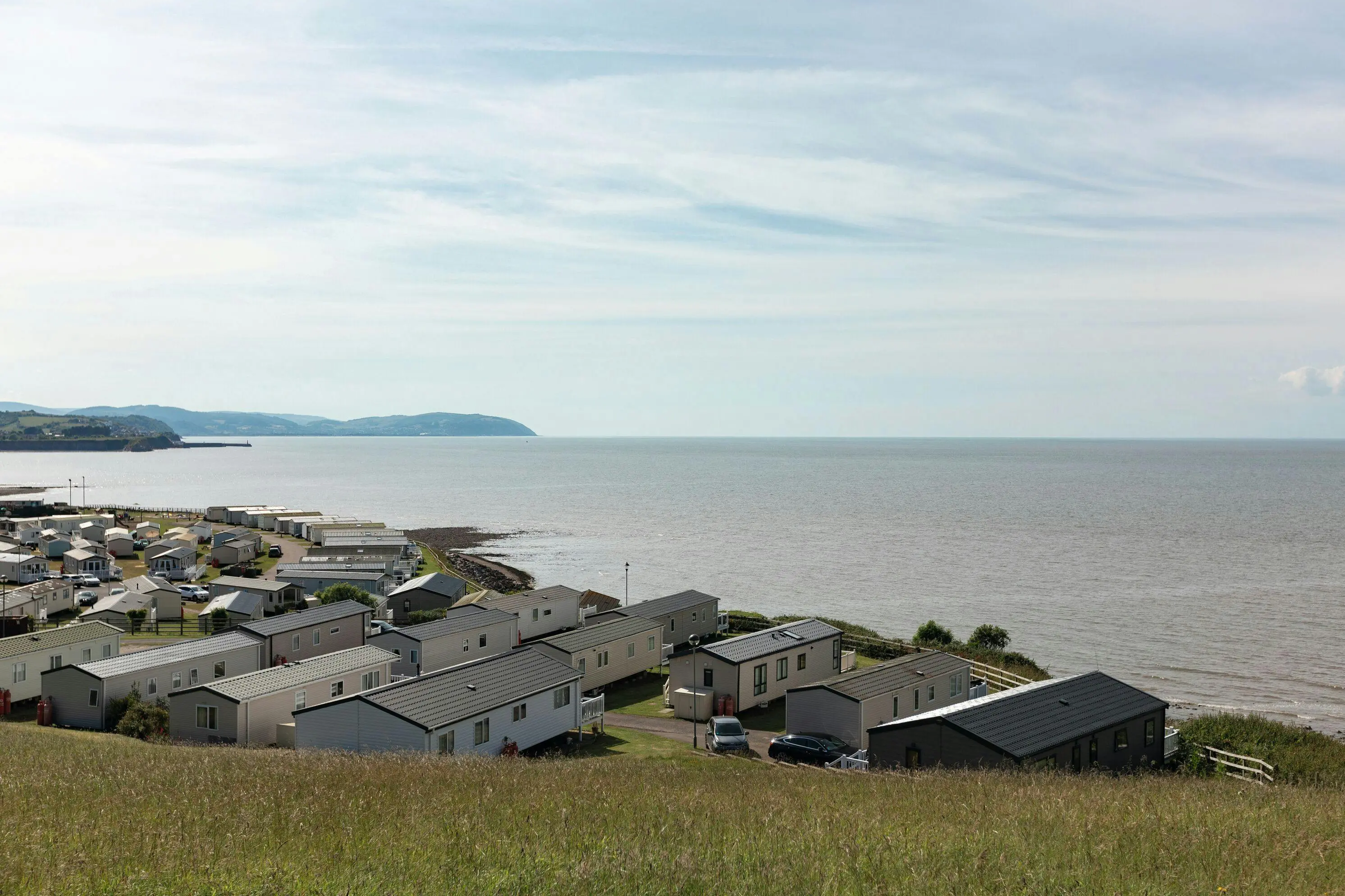 A coastal caravan park with rows of holiday homes overlooking the ocean under a cloudy sky.