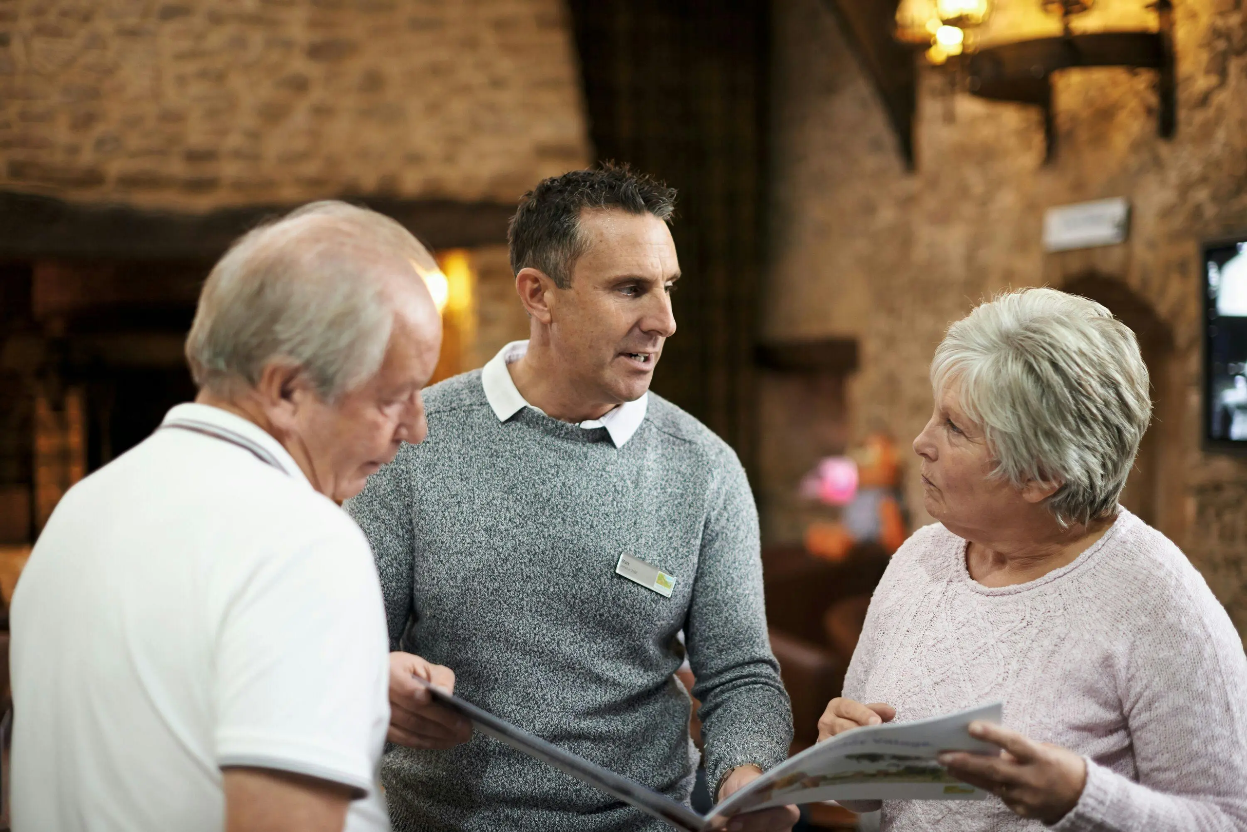 A sales representative discusses a brochure with an older couple in a rustic indoor setting.