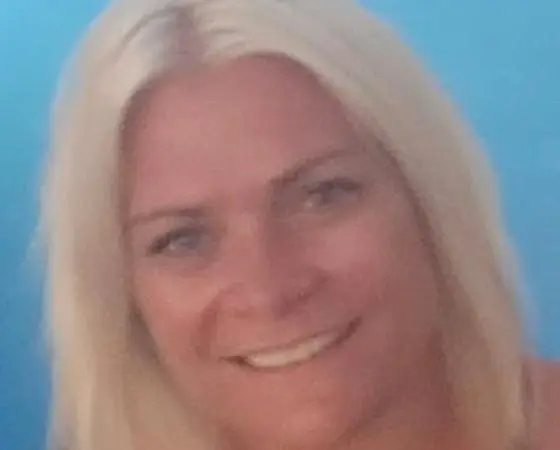 A close-up portrait of Helen Aikman with blonde hair against a light blue background.