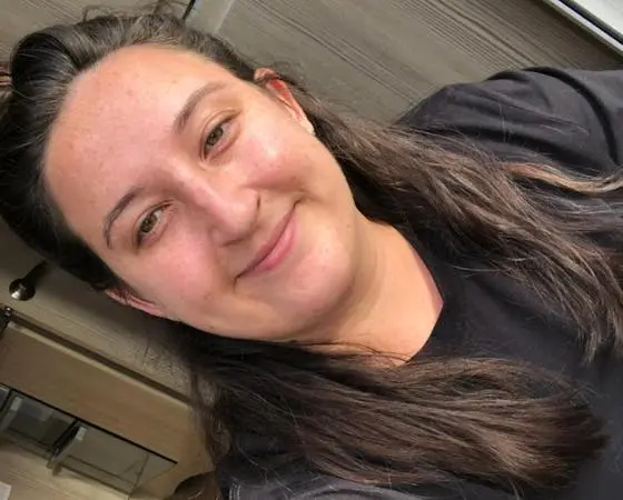 A woman with long brown hair smiling at the camera, wearing a black shirt.