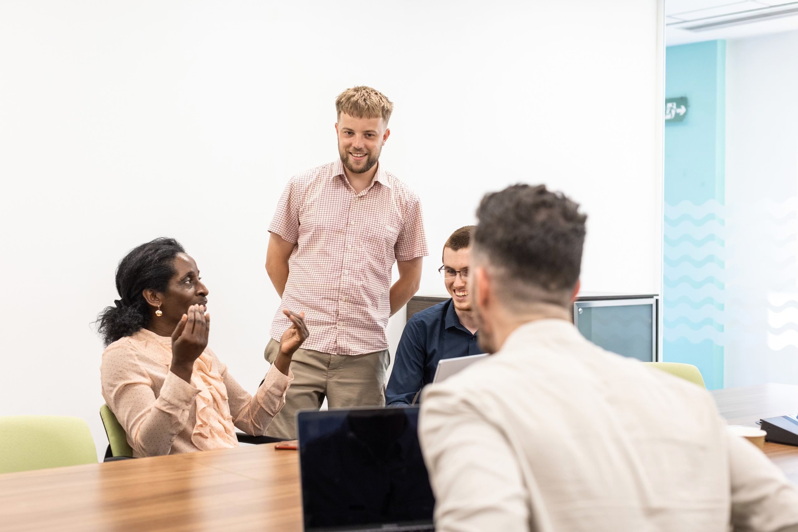 A diverse group of colleagues collaborating and discussing work in a bright, modern meeting room.