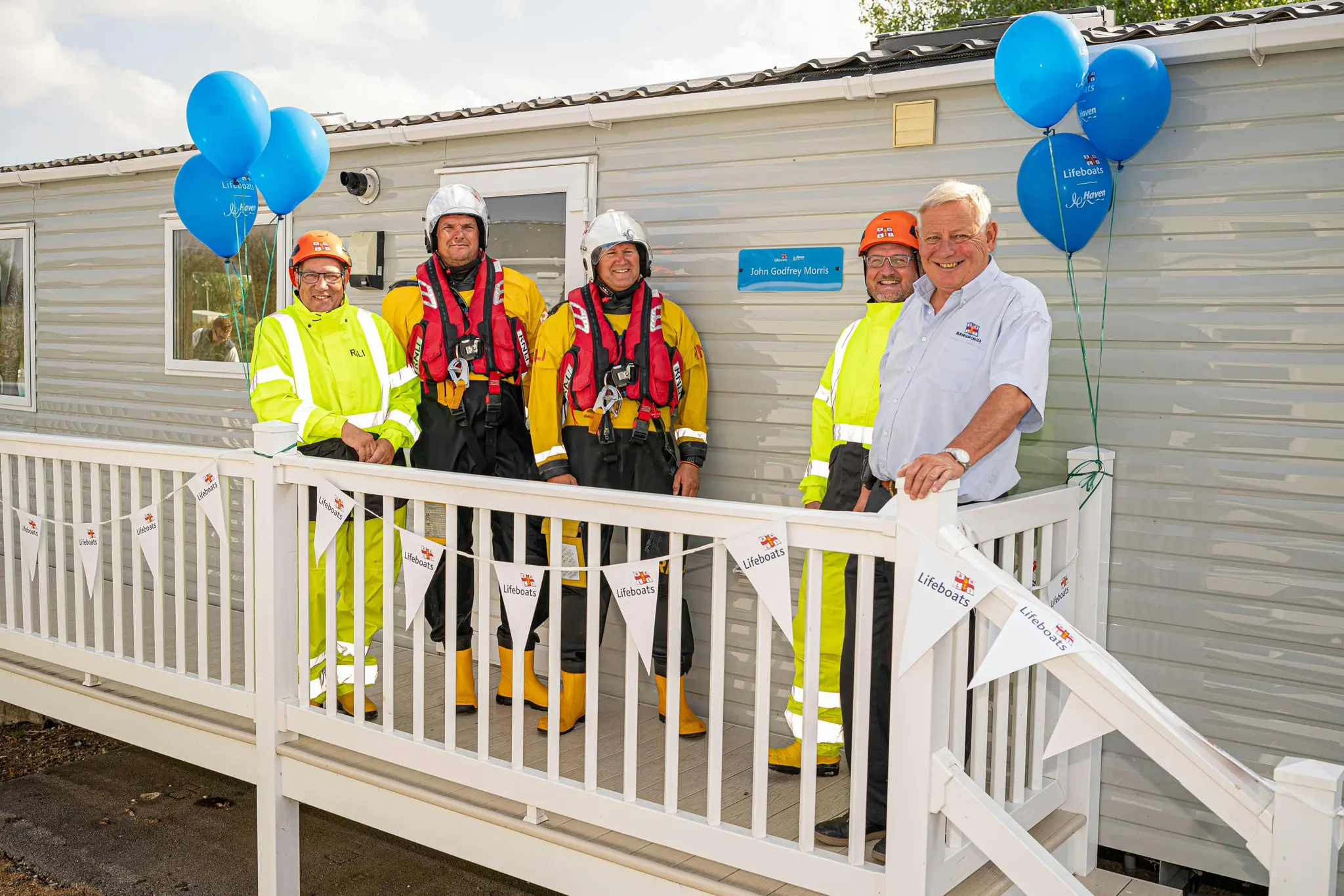 Five men, including four RNLI crew members in gear, pose on a decorated deck with balloons.