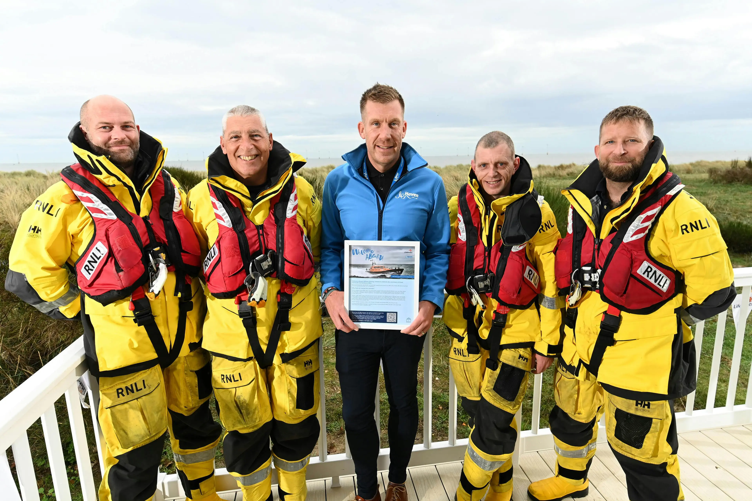 Five RNLI crew members in yellow gear and a man holding a framed certificate outdoors.