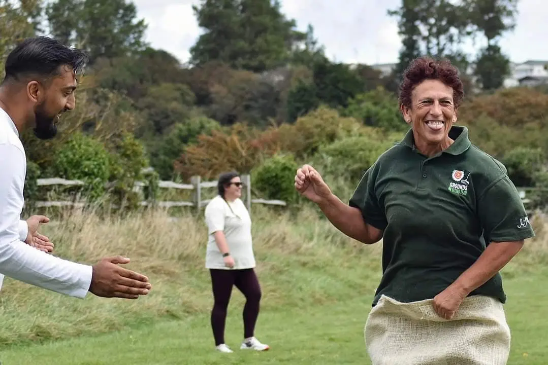 A woman playfully participating in a sack race at an outdoor sports day event, with spectators watching.
