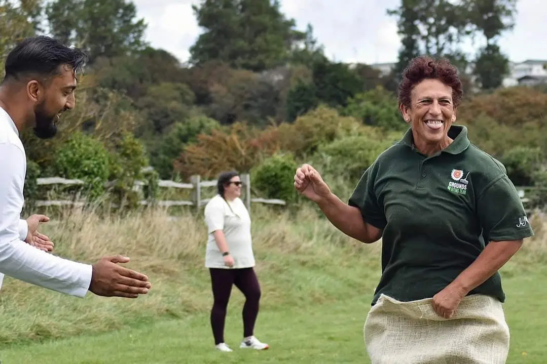 A woman playfully participating in a sack race at an outdoor sports day event, with spectators watching.