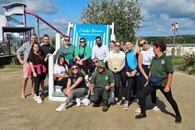 A large group of adults posing together outdoors on a sunny day near a water park attraction.