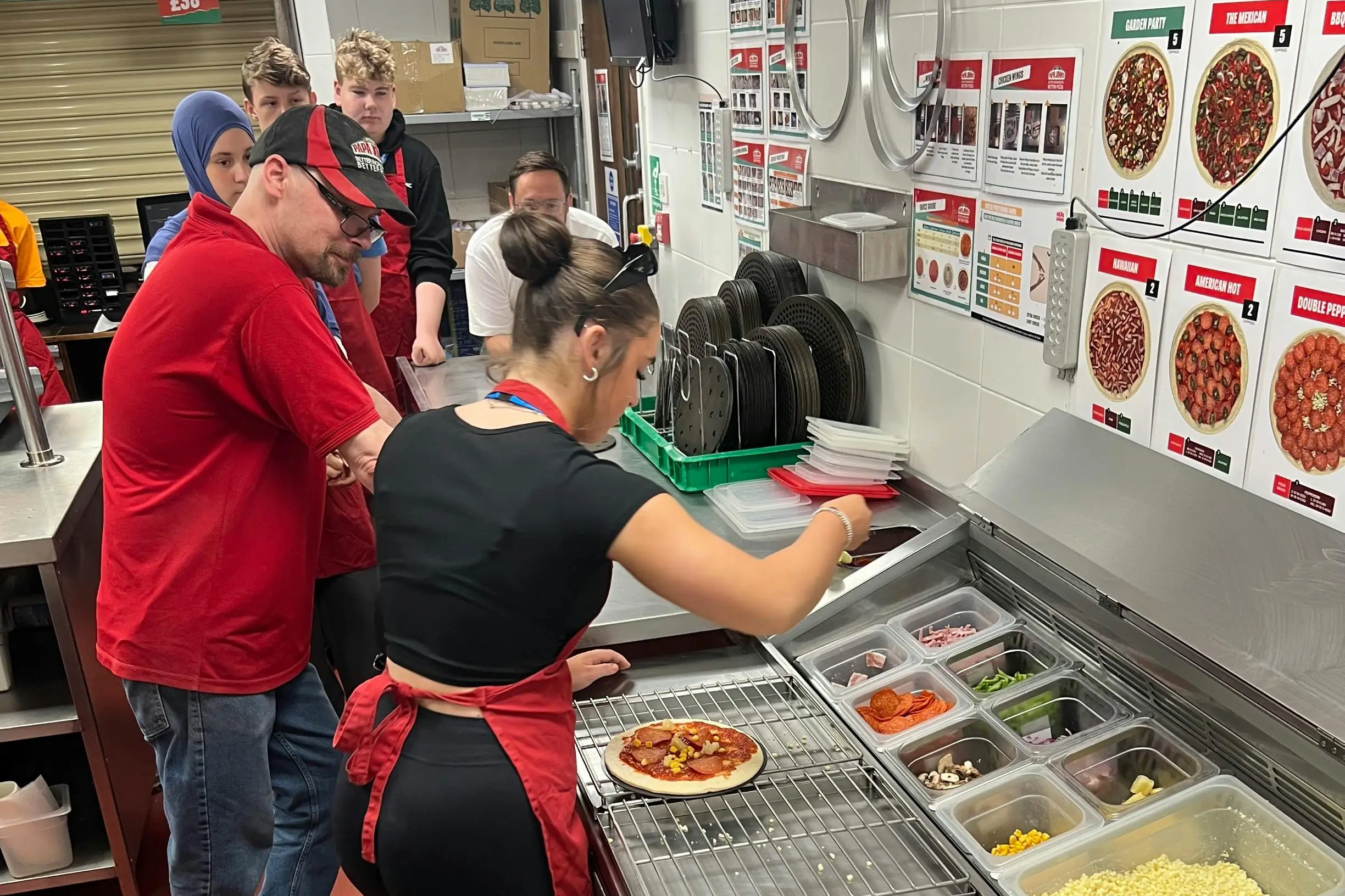 A group of trainees learning to make pizza at a kitchen prep station.