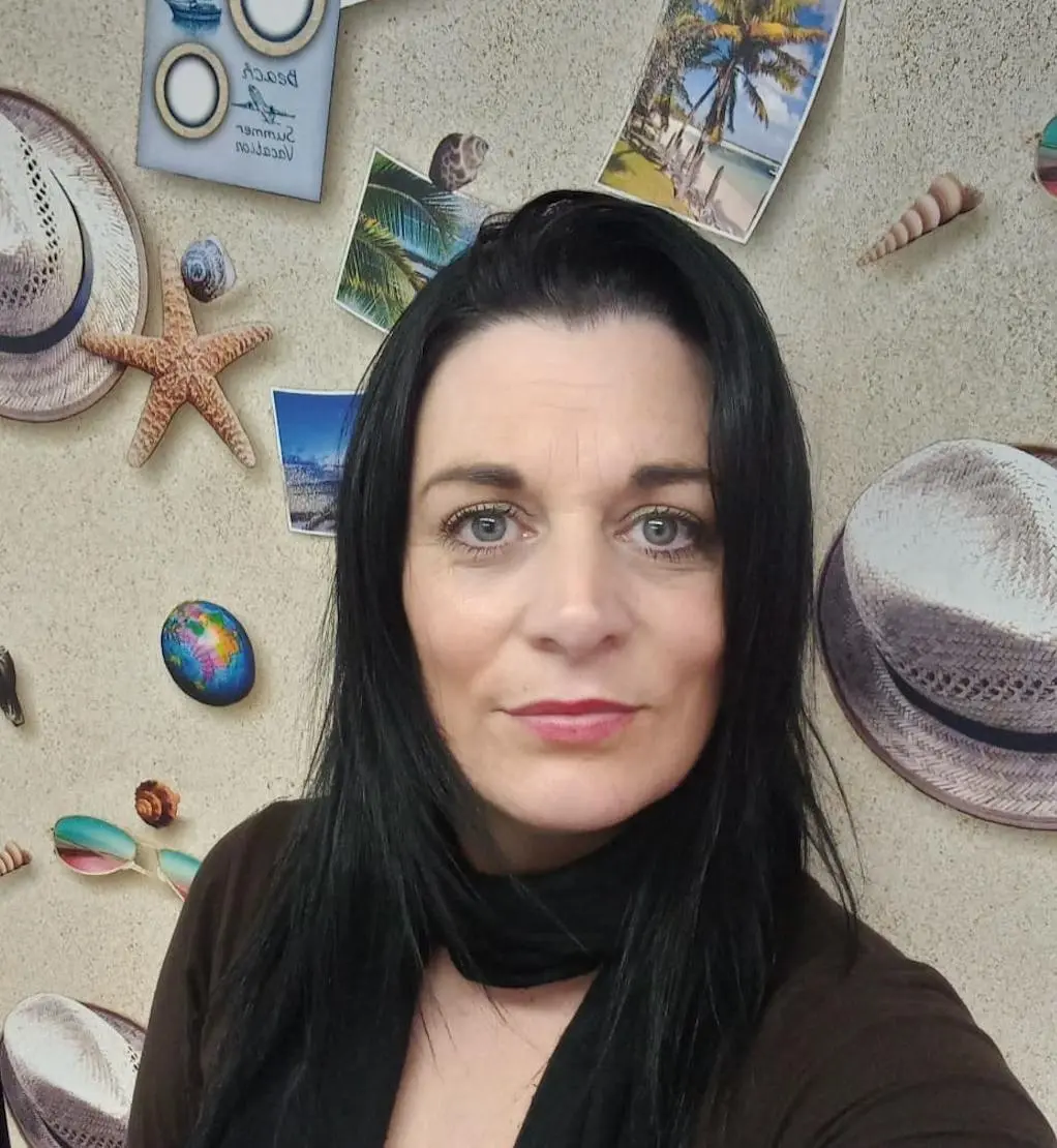 A woman with black hair posing in front of a wall decorated with vacation-themed items.