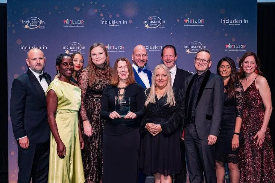 Ten people posing together at the Inclusion Awards event in front of a branded backdrop.