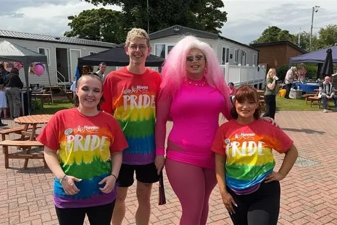Four people posing outdoors in pride shirts, including one in a bright pink outfit.
