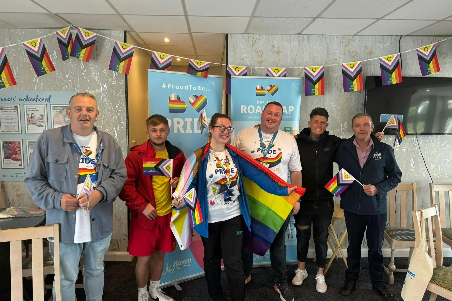 Six people holding pride flags and banners indoors, celebrating inclusivity.
