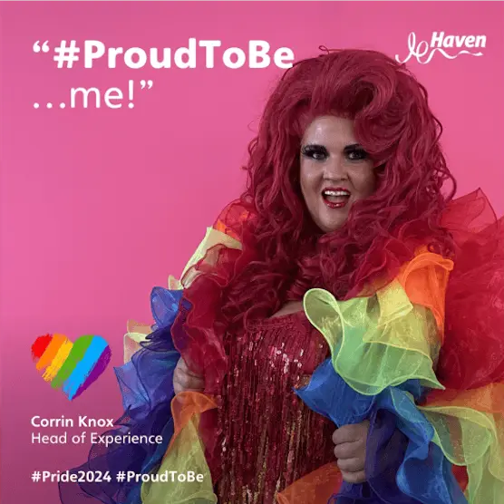 Corrin Knox with red hair and a rainbow ruffled dress, in front of a pink background for Pride.