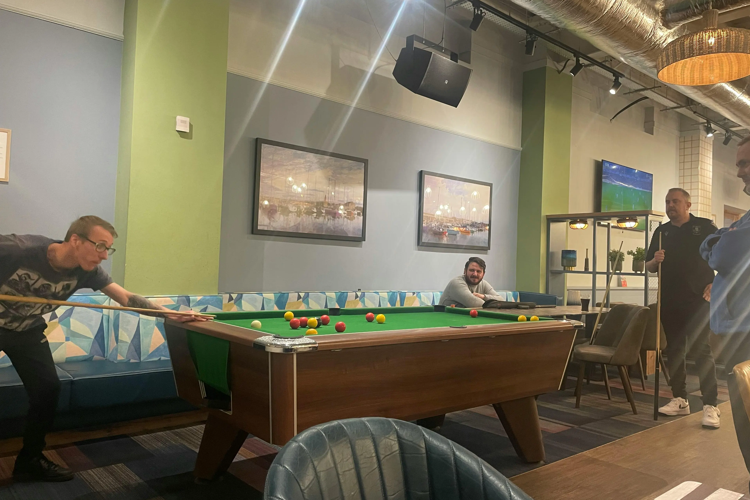 A group of men gathered around a pool table in a pub, with one person lining up a shot.