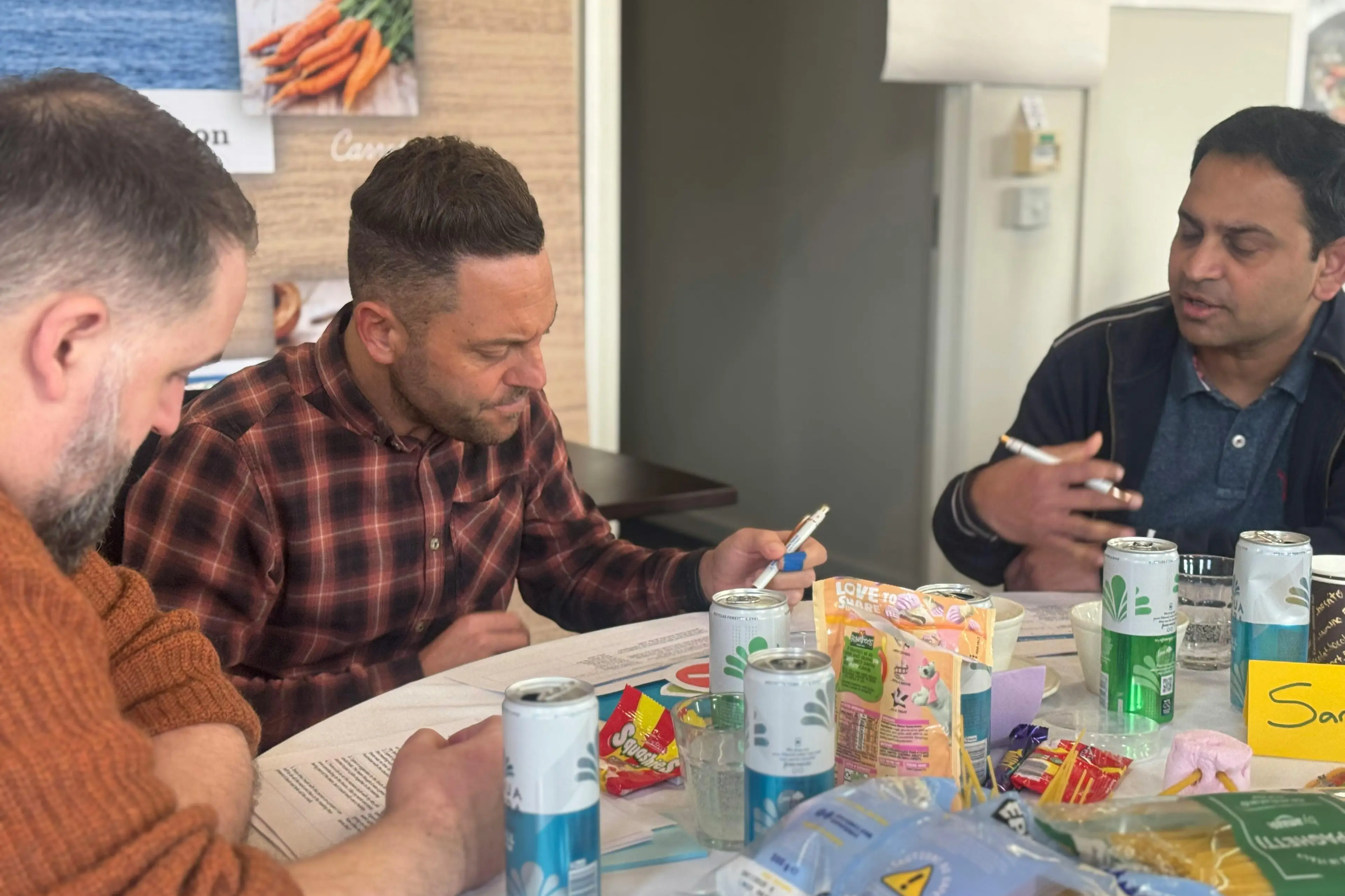 Three men sitting around a table with drinks and snacks during a meeting