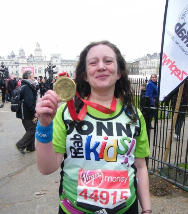 Donna O'Toole smiling while holding up her London Marathon medal outdoors.