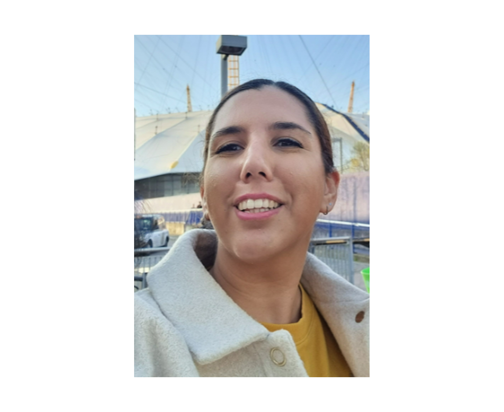 A woman smiling outdoors with a large tent structure in the background.