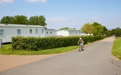 A young child rides a bicycle along a paved path past mobile homes.
