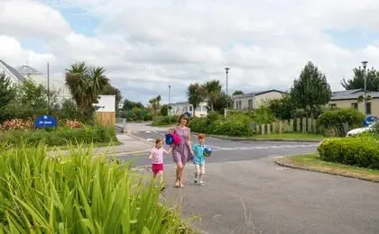 A woman and two children walking along a paved path in a holiday park surrounded by mobile homes.