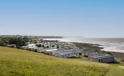 An elevated view of a coastal holiday park with many static caravans near the sea and grassy hills.