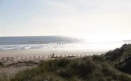 A wide sandy beach meeting the ocean under a bright, overcast sky with dunes in the foreground.