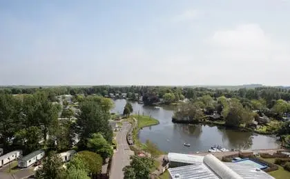 High-angle view of a resort with a lake, pathways, and surrounding trees under a bright sky.