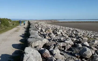 People walking along a coastal path beside a rocky breakwater and a calm sea.