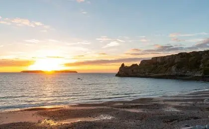 A peaceful coastal view during sunset with gentle waves meeting a rocky shore.