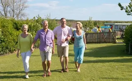 Two older couples walking together on a grassy lawn on a sunny day.