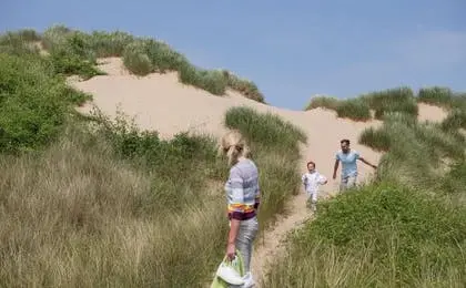 A family walking through grassy sand dunes on a sunny day.