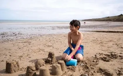 A young boy smiling while building sandcastles on a scenic beach.