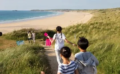 Children walking down a path through grassy dunes towards a scenic sandy beach and ocean.