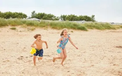A young boy and girl running happily across a sandy beach with buckets.