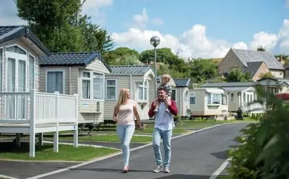 A family walking together through a holiday park lined with static caravans on a sunny day.