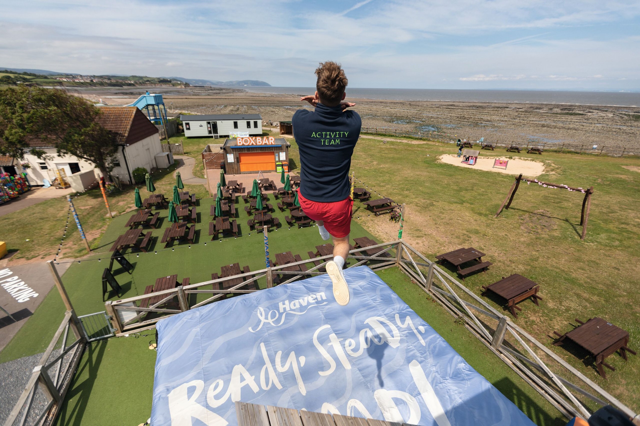 An Activity Team member jumps from a high platform toward a large inflatable landing bag below.
