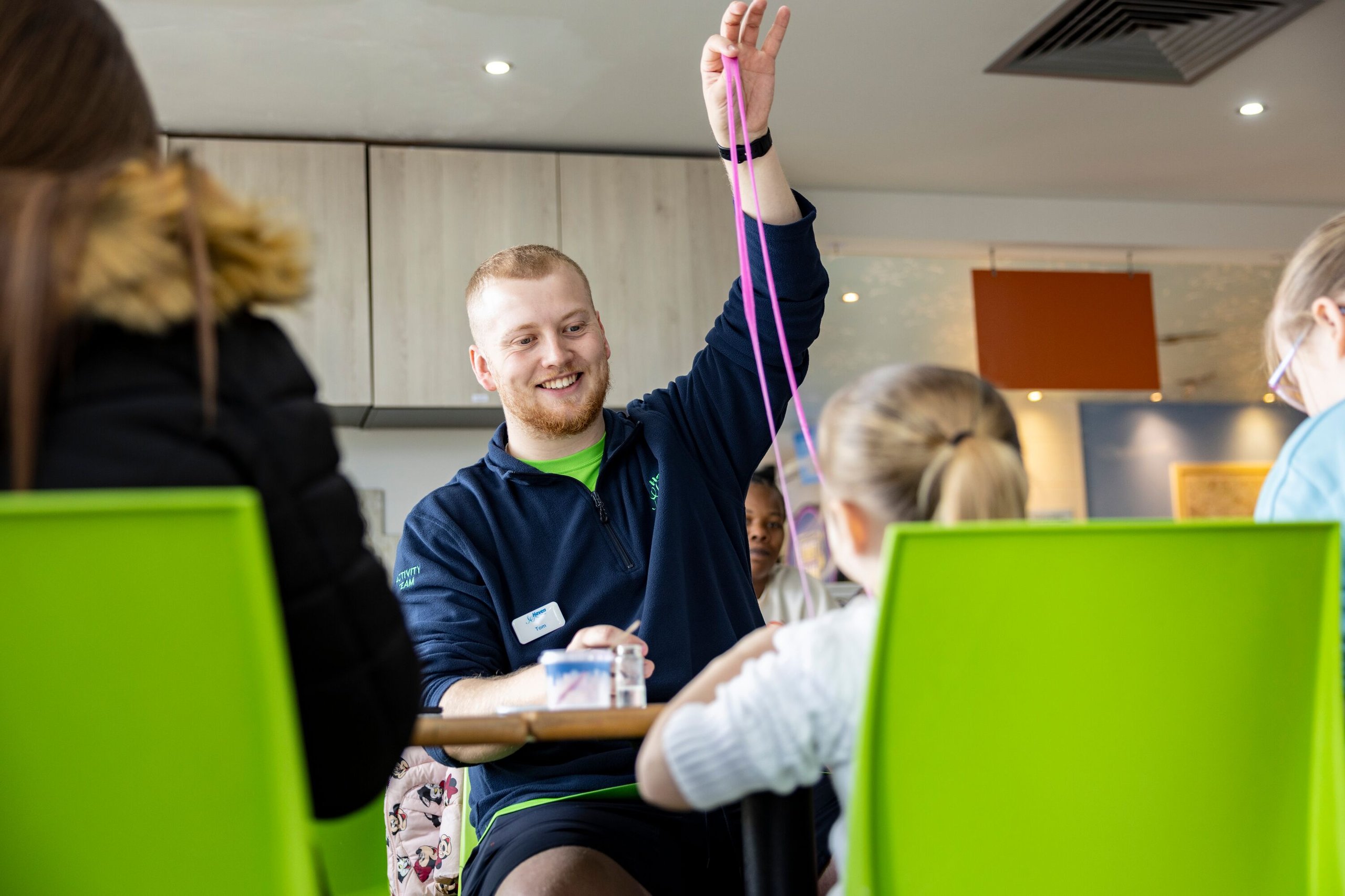 An activity leader smiling while holding up a long strand of pink slime for children.