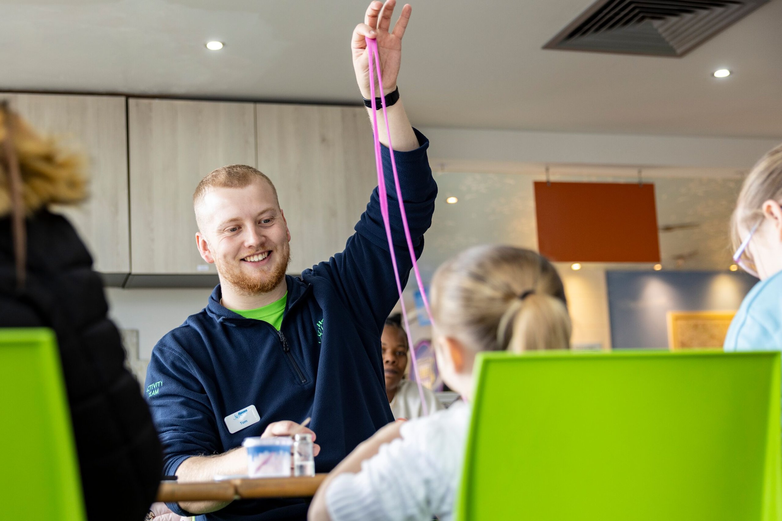 An activity leader smiling while holding up a long strand of pink slime for children.